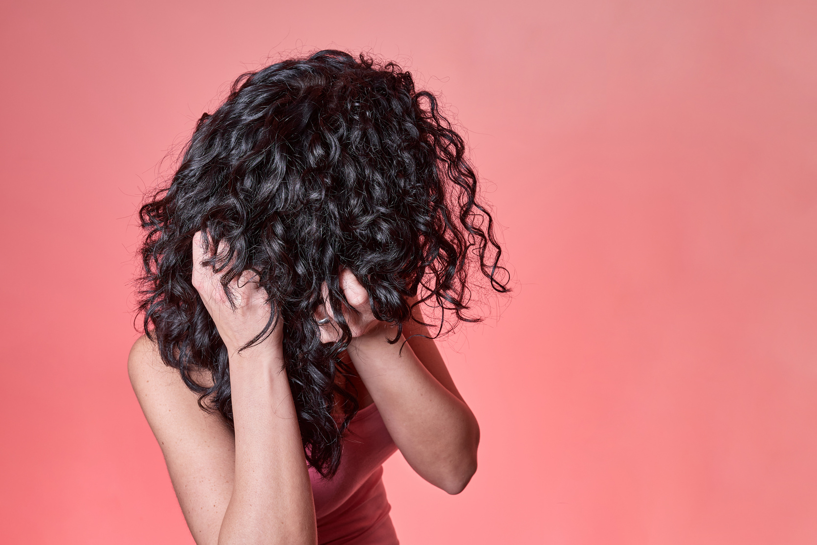 young black curly haired woman combing her hair following curly girl method on pink background. hair care concept.